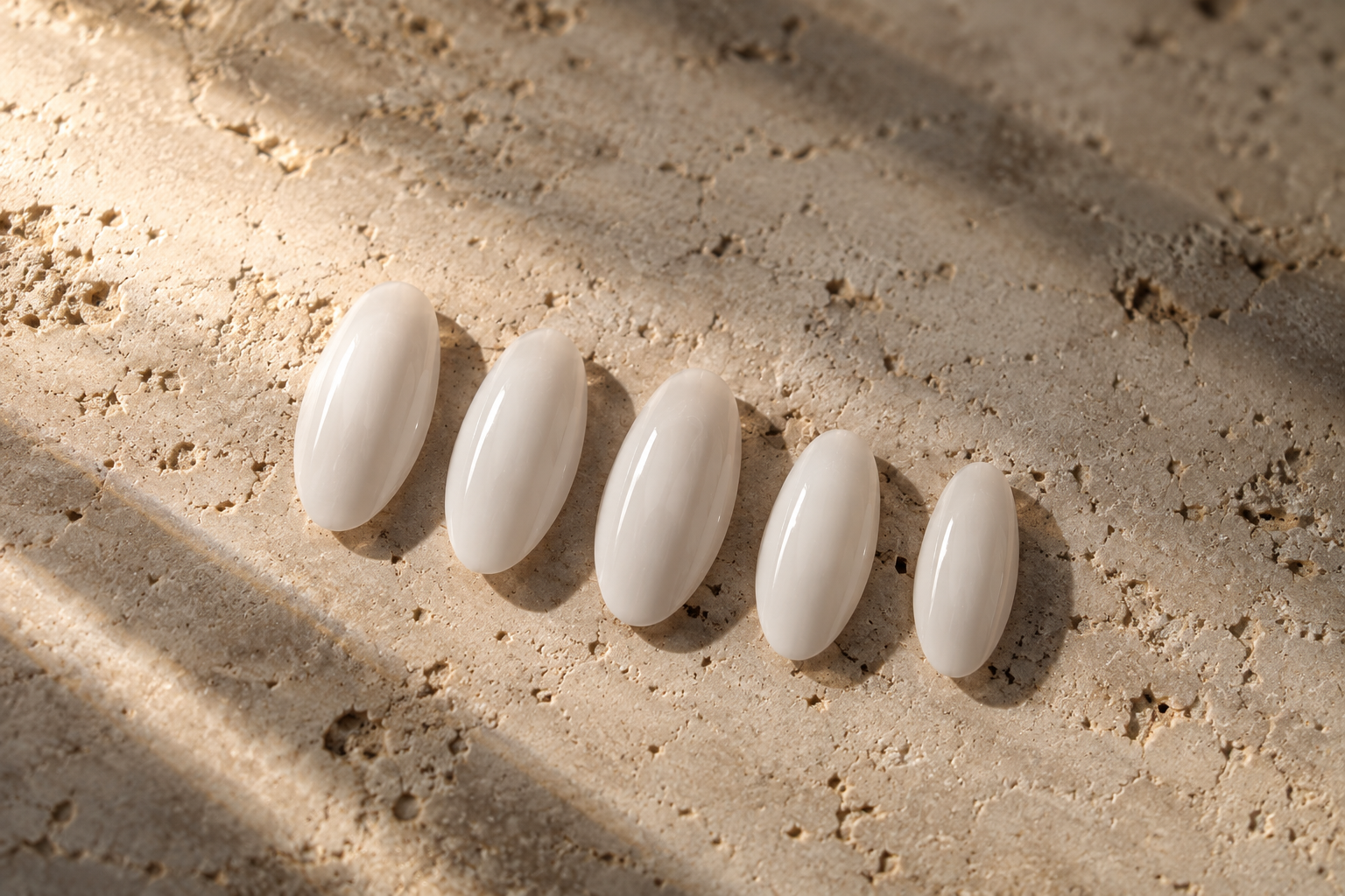 SET. 001 MILK milky-white almond press-on nails photographed on warm ivory travertine.