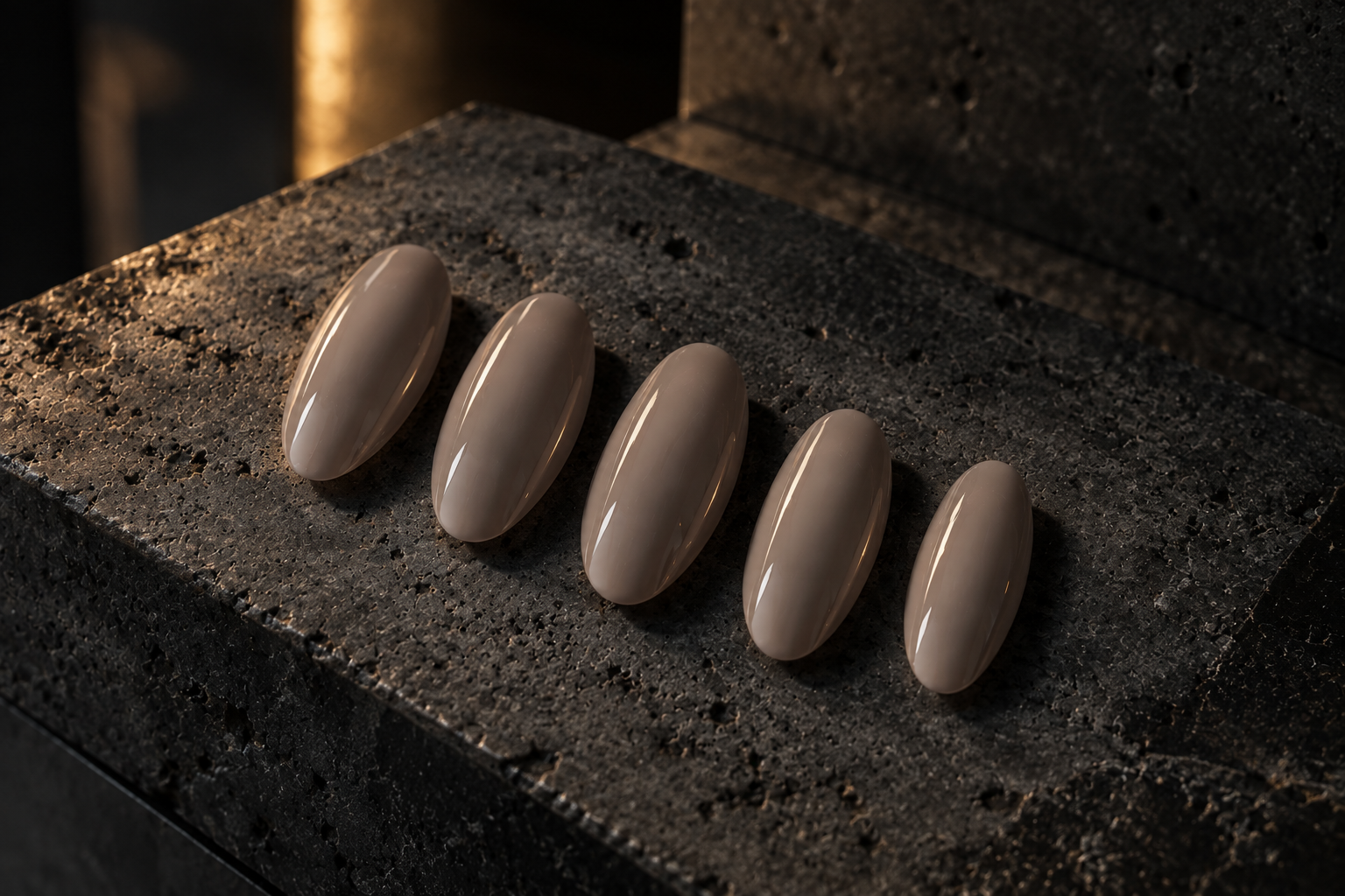 SET. 003 TAUPE taupe-gray almond press-on nails photographed on dark architectural stone.