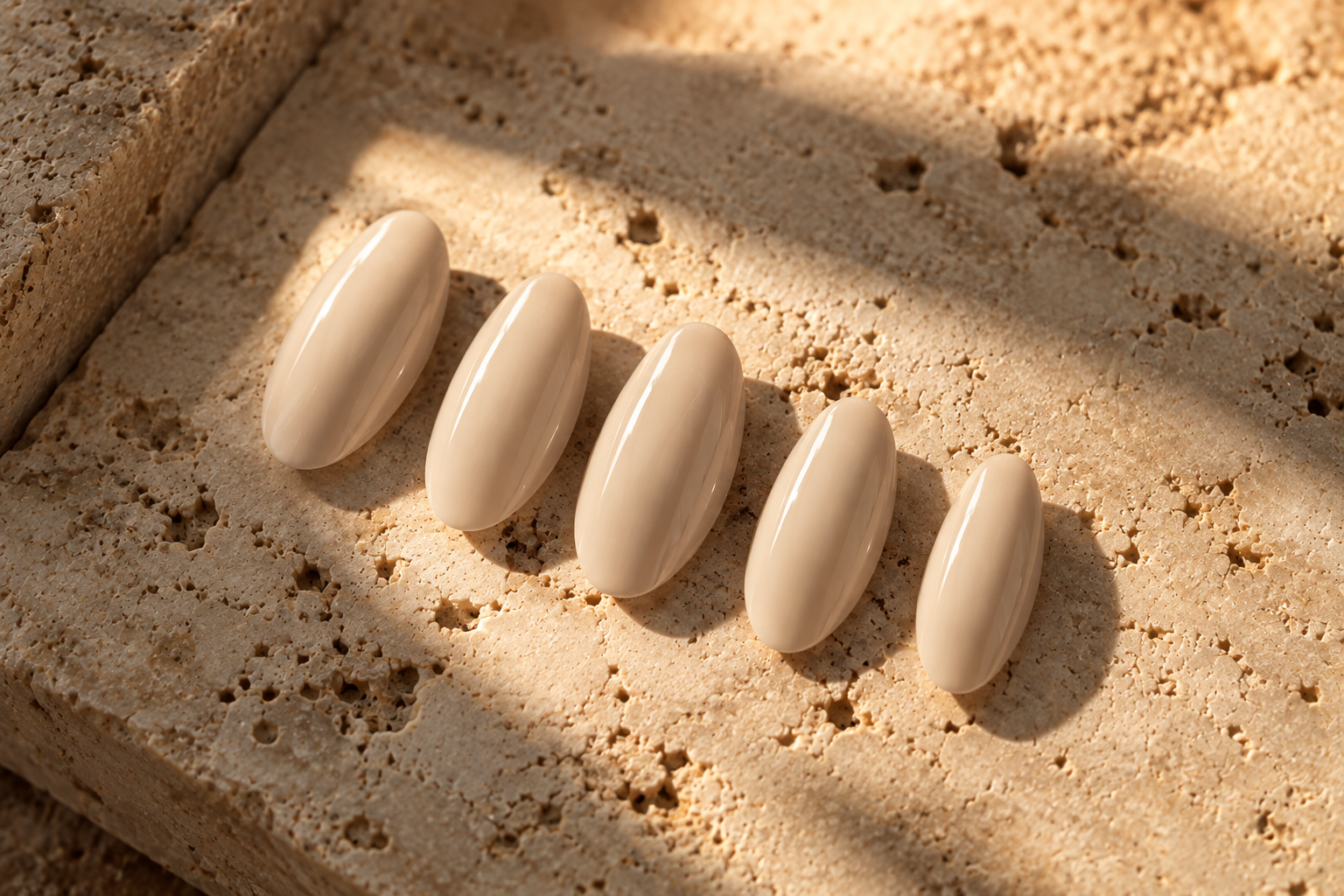 SET. 002 BONE warm bone almond press-on nails photographed on sunlit travertine.