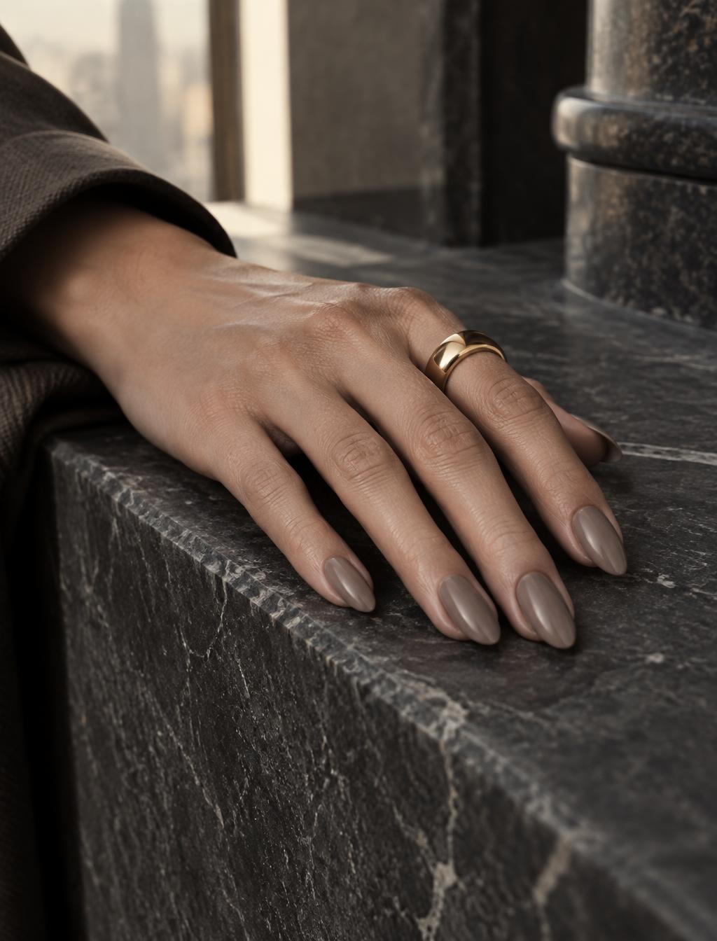 Hand resting on dark architectural stone wearing SET. 003 TAUPE taupe-gray almond nails.
